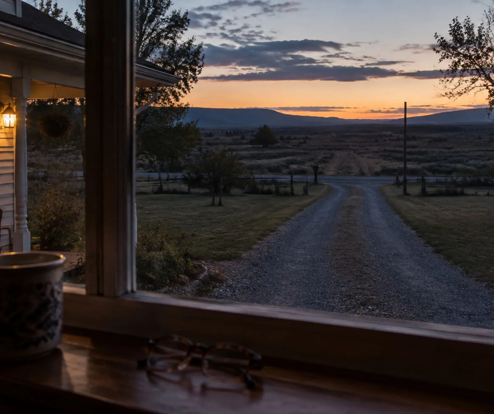 The gravel drive at dusk, seen from a front window with the porch light on